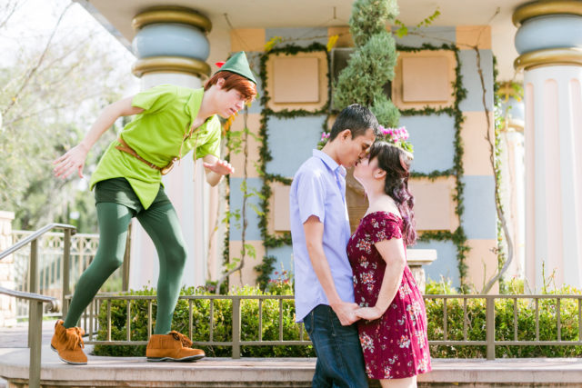 Couple posing for engagement photos in Fantasyland at Disneyland with Peter Pan photobomb