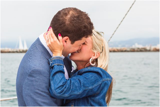 Man on bended knee on sailboat in marina proposing to girlfriend