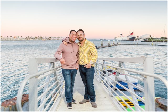 Grooms posing for engagement session on rock cliff overlooking the marina in Long Beach at sunset.