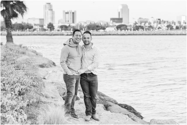 Grooms posing on rock cliff overlooking the marina in Long Beach at sunset.