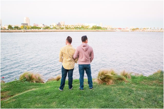 Two grooms posing on rock cliff overlooking the marina in Long Beach at sunset.