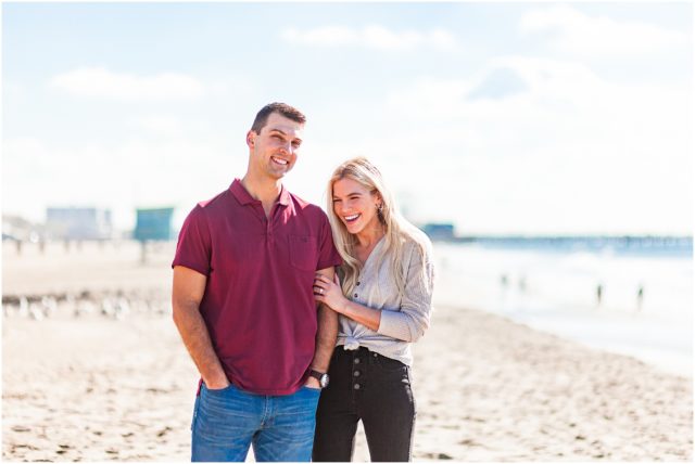 Newly engaged couple holding hands and laughing on beach