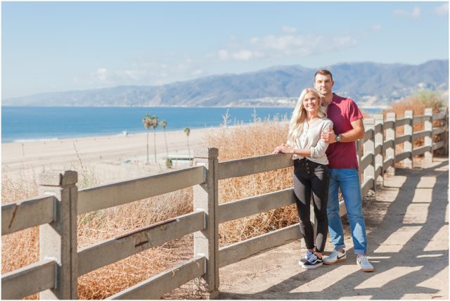 Newly engaged couple posing at their surprise beach engagement session in Santa Monica with Malibu in background